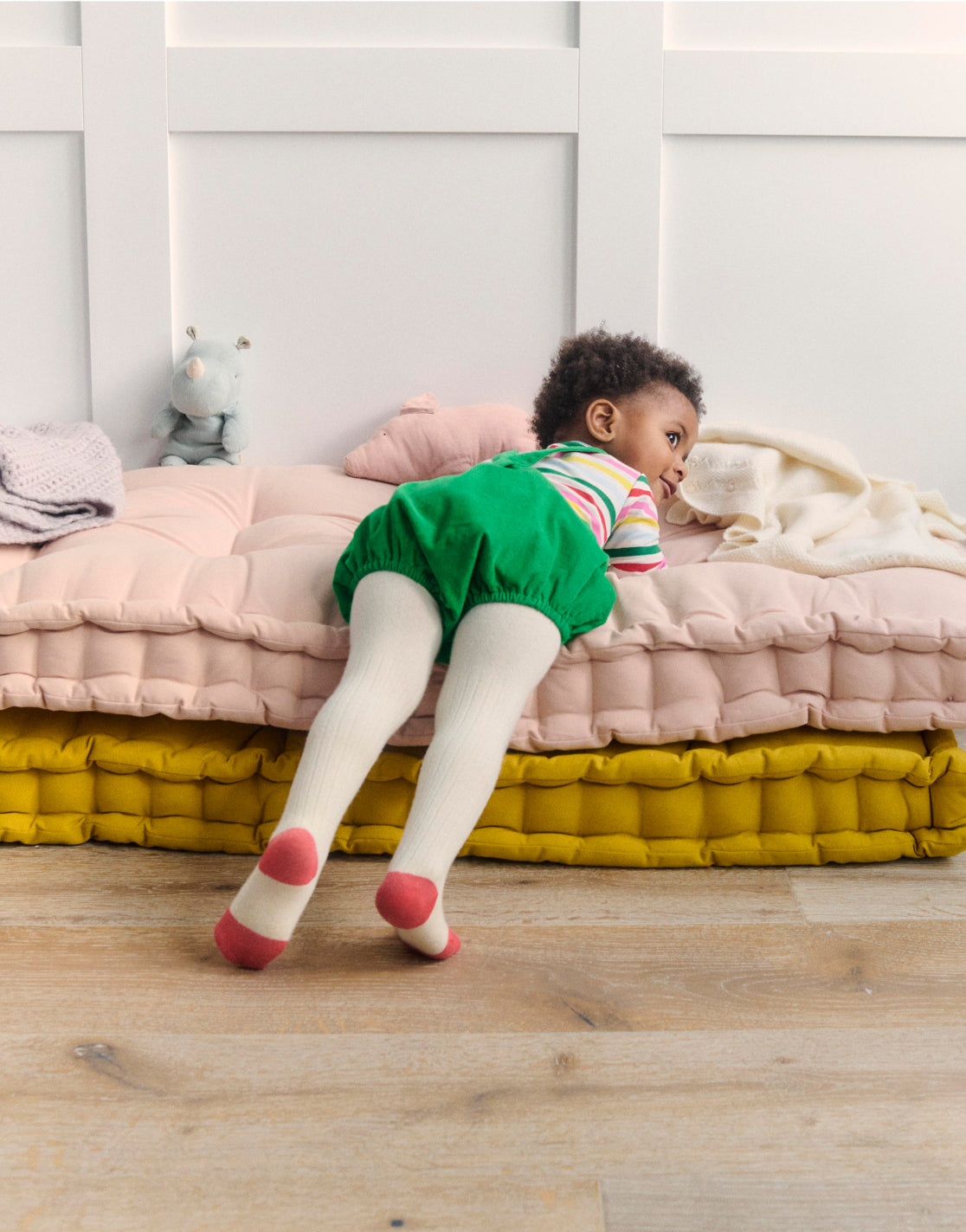 Baby lying on cushions wearing colourful Boden clothes