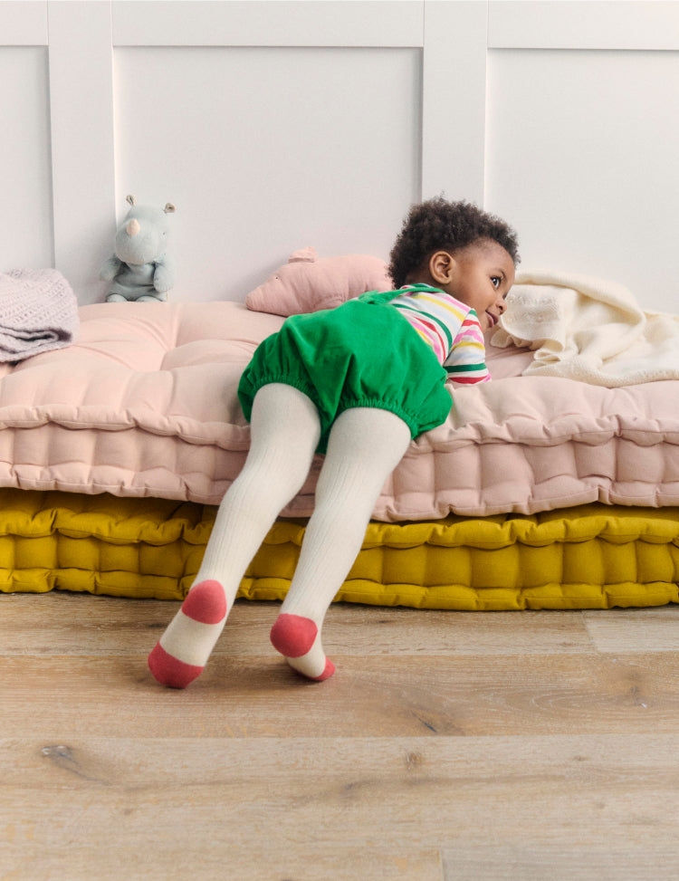 Baby lying on cushions wearing colourful Boden clothes