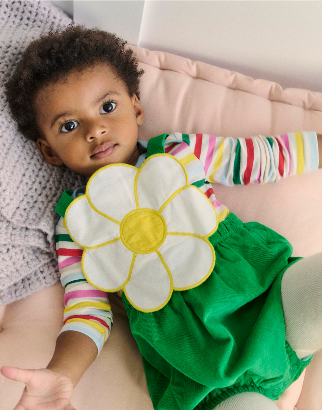 Baby lying down, wearing Boden novelty flower romper