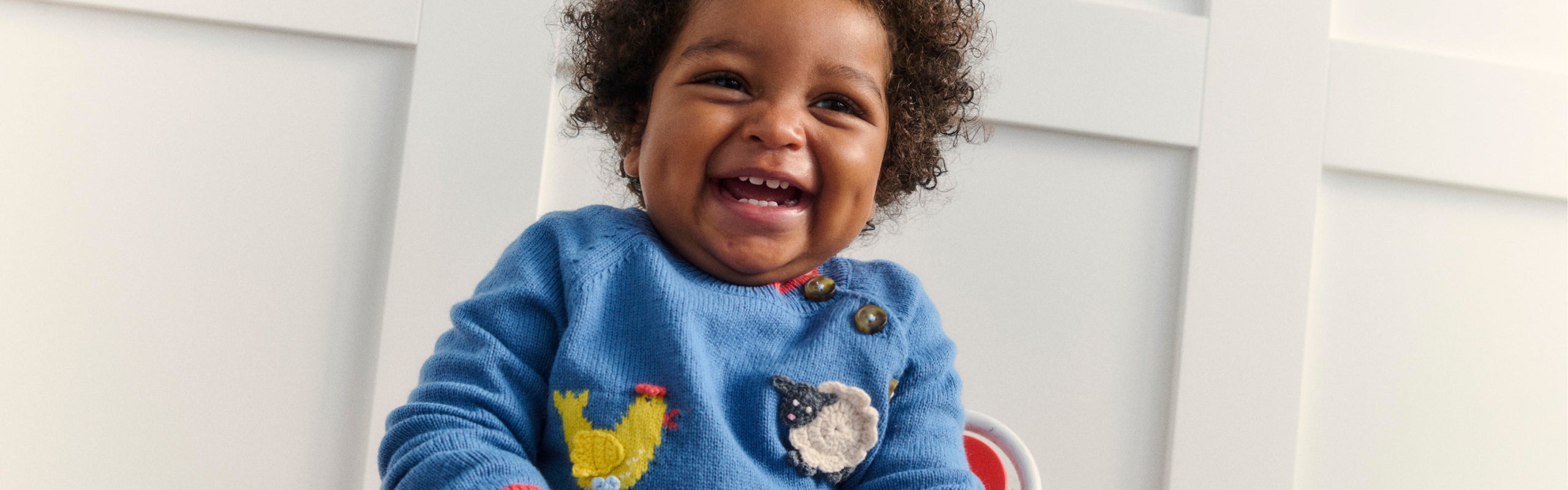 Baby laughing and wearing Boden knitwear and trousers