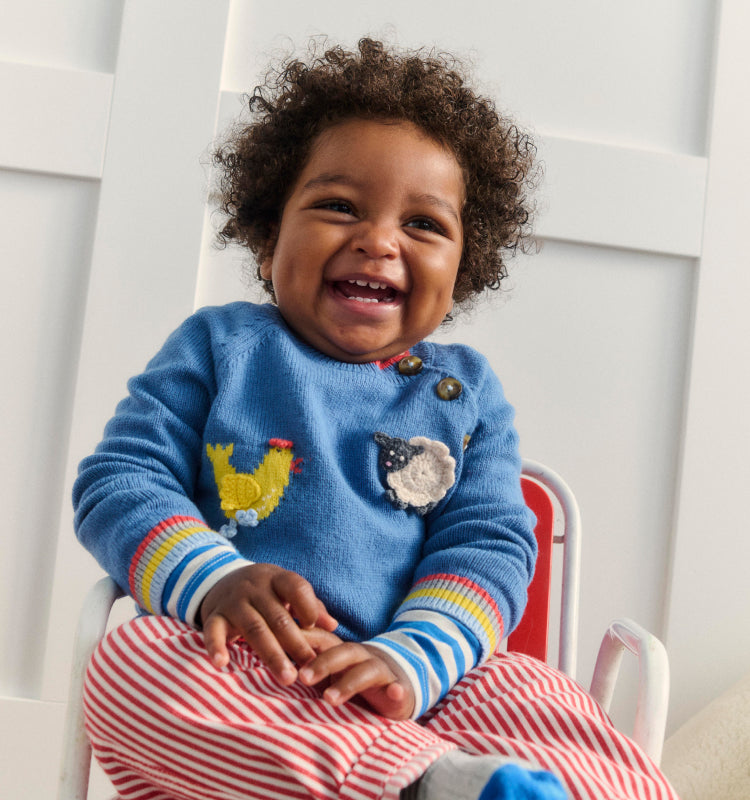 Baby laughing and wearing Boden knitwear and trousers