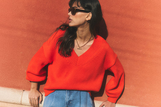 Eine Person, die einen knallroten Pullover und eine Sonnenbrille trägt, vor einer roten Wand.