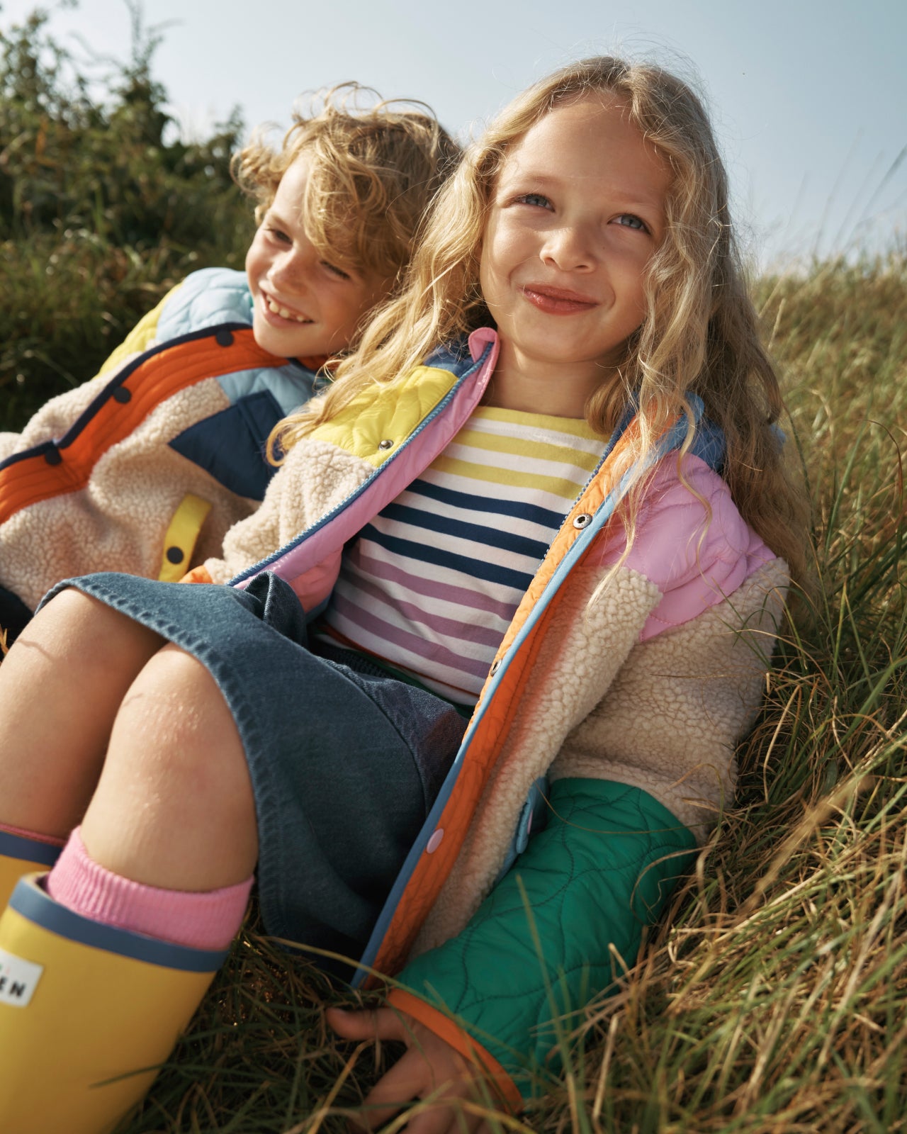 Girl sat in a field wearing colourful Boden borg coat