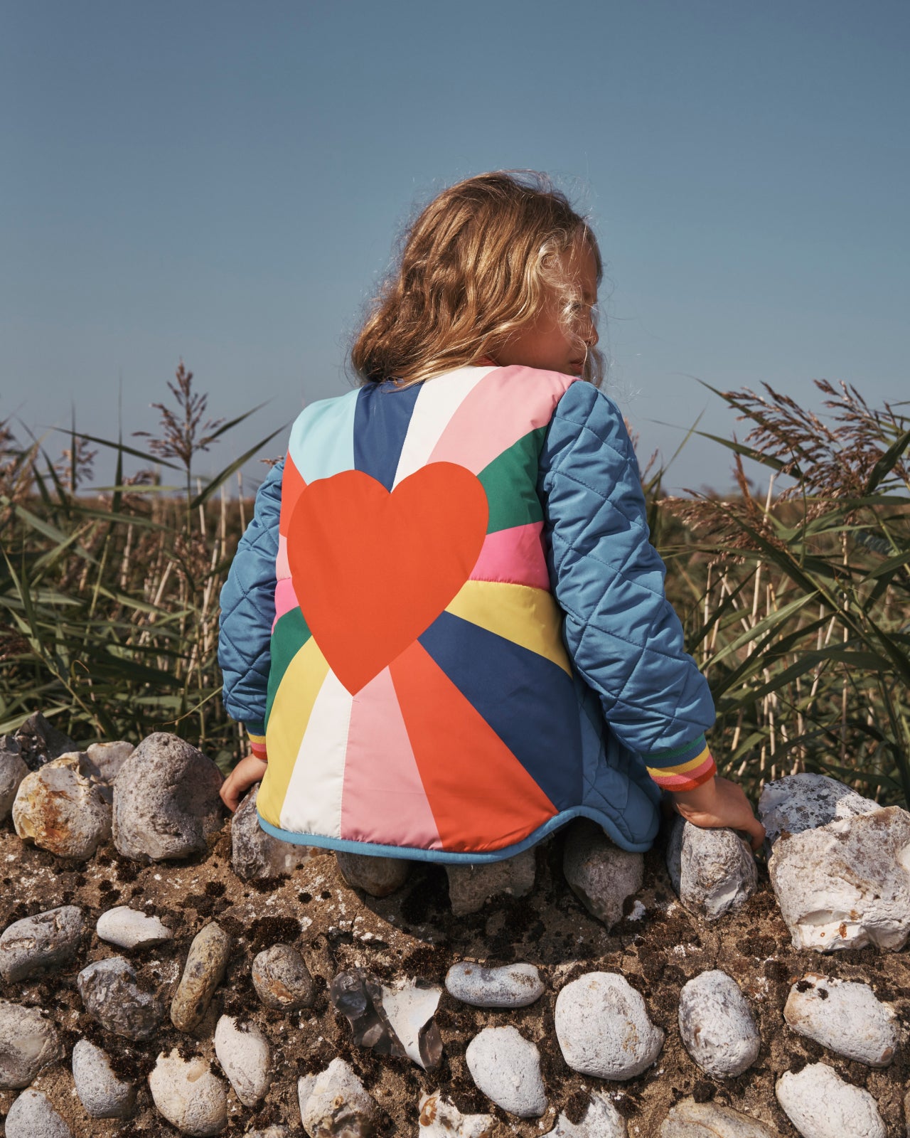 Girl sat on a wall, showing the colourful back of a Boden coat