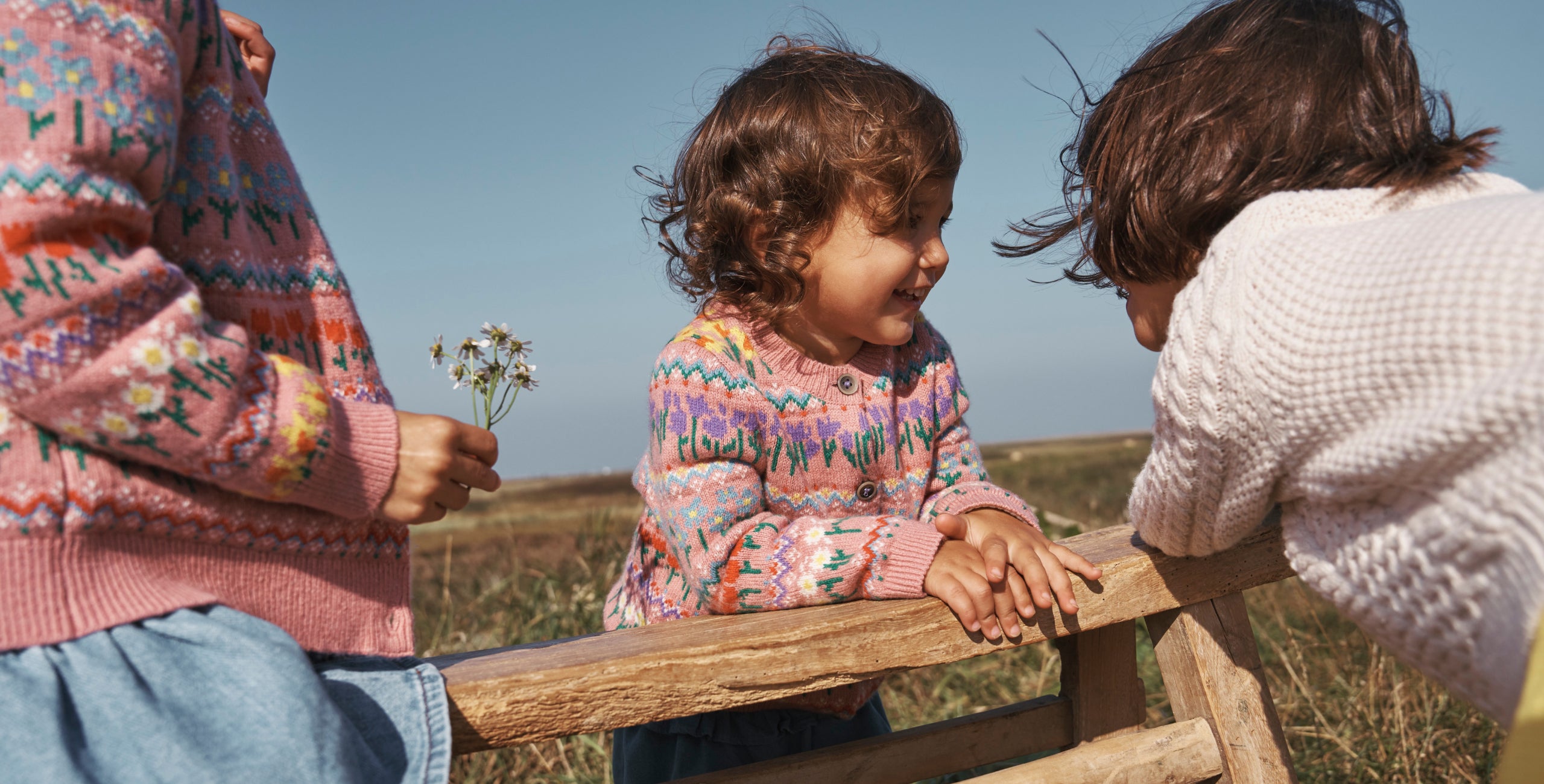 Three girls in a field wearing Boden knitwear