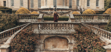 Eine Frau in einem Cordanzug, die oben auf der Treppe vor einem Schloss steht