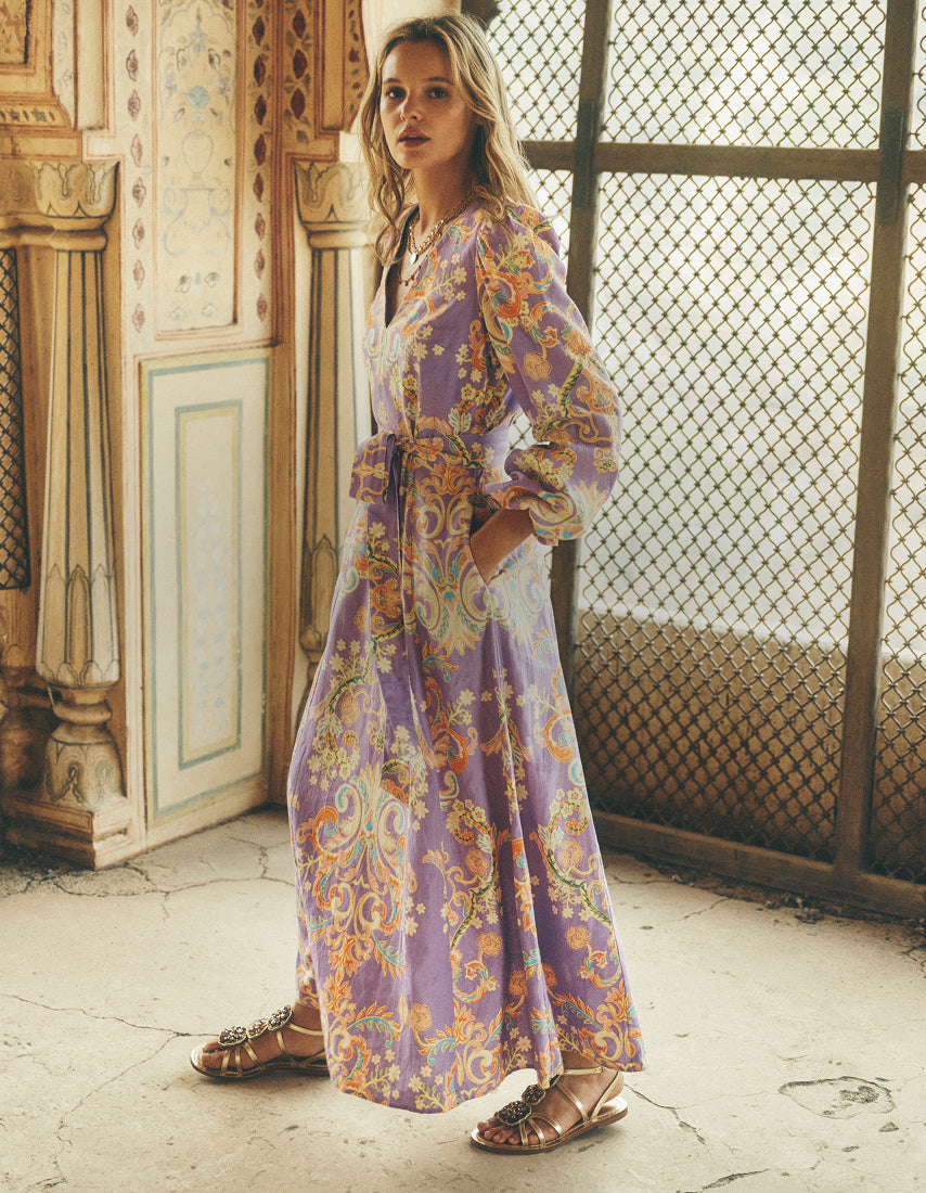 Eine Frau in einem langen, gemusterten Kleid steht in einem Raum mit dekorativen Elementen.