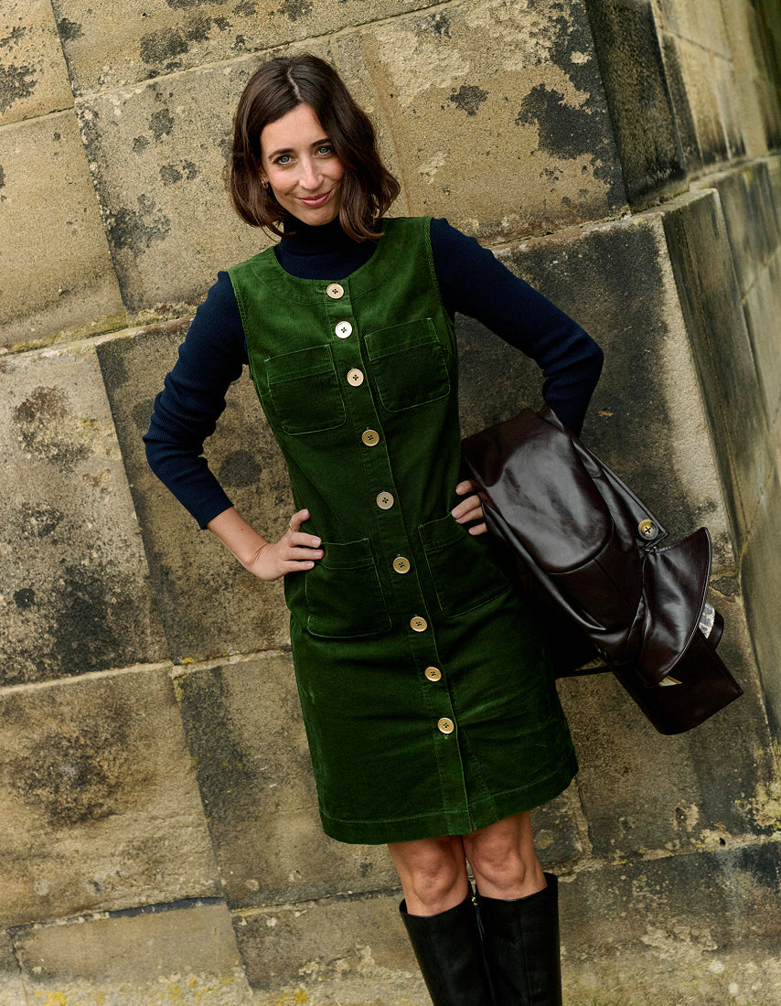 Frau in einem grünen Cordkleid vor einer Steinmauer
