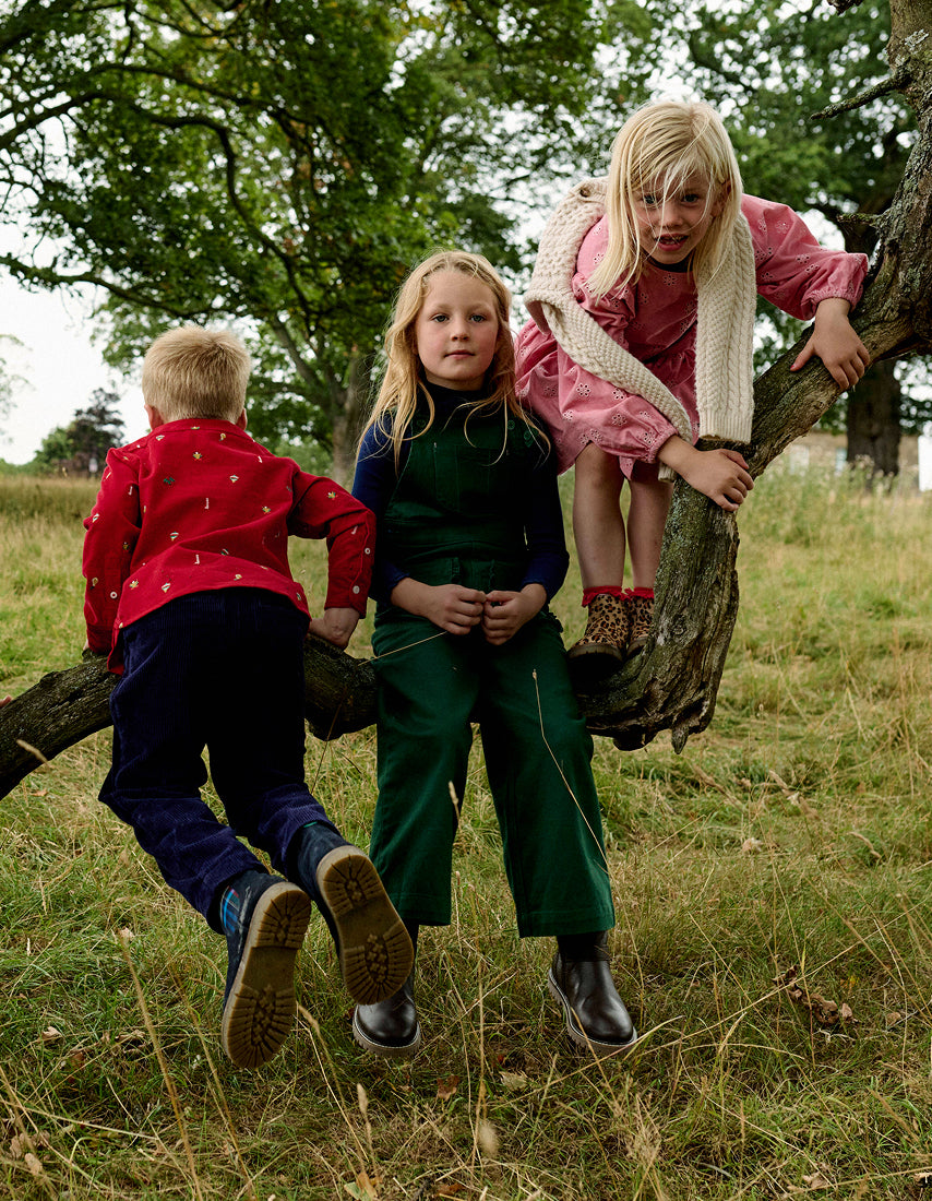 Three children playing on a tree branch in a grassy field.