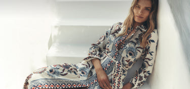 Eine Frau in einem gemusterten Kleid sitzt auf einem weißen Sofa.