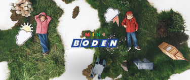 Ein Kinderspielset oder eine Miniaturszene mit zwei Kindern, die auf einer Wiese liegen, mit Spielzeugwolken, einem kleinen Boot und dem Schriftzug „MINI BODEN“ in der Mitte.