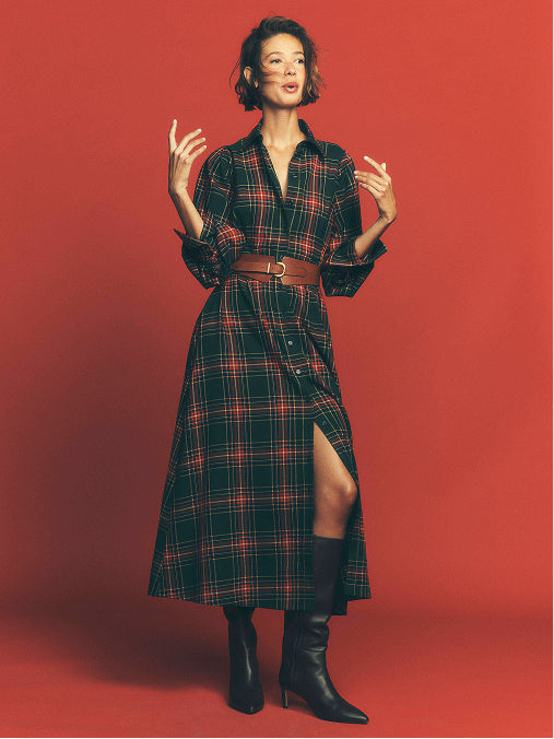 Eine Frau in einem roten Tartan-Hemdkleid, die vor einem roten Hintergrund steht.