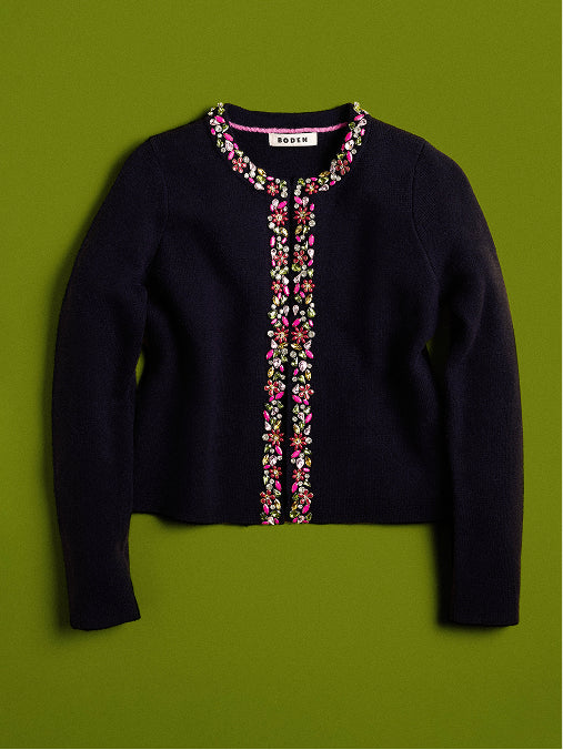 Ein dunkelblauer Strickcardigan mit bunten Blumenstickereien auf der Vorderseite und rund um den Kragen, flach auf einem einfarbigen olivgrünen Hintergrund präsentiert.