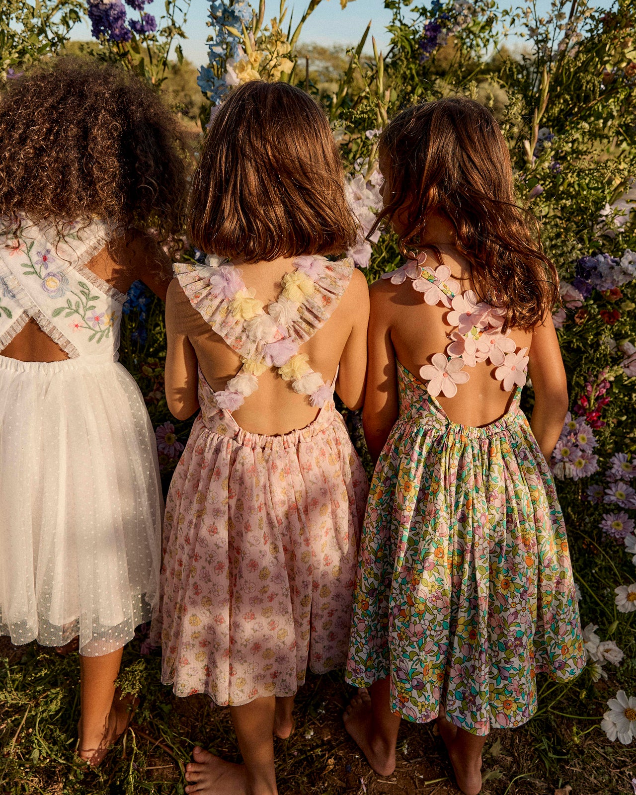 Three young girls in floral dresses standing in a field of flowers.
