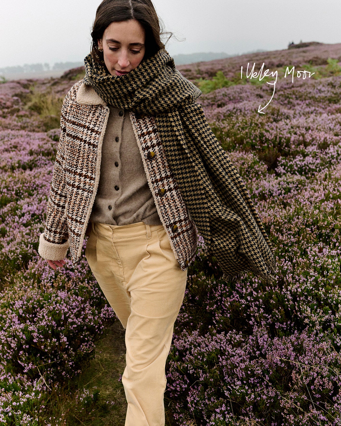 Frau mit gemustertem Schal und Mantel in einem Feld voller violetter Blumen