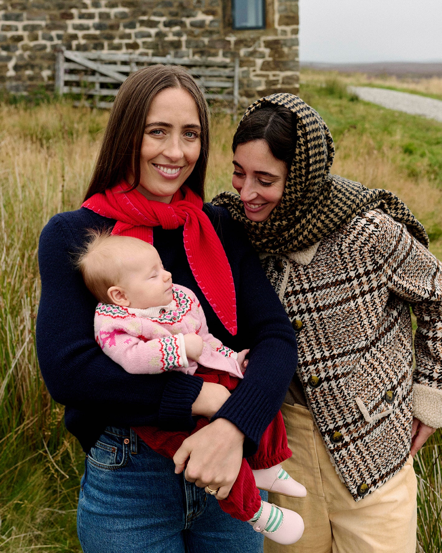 Zwei Frauen stehen mit einem Baby im Freien, eine hält das Baby, in einer natürlichen Umgebung.