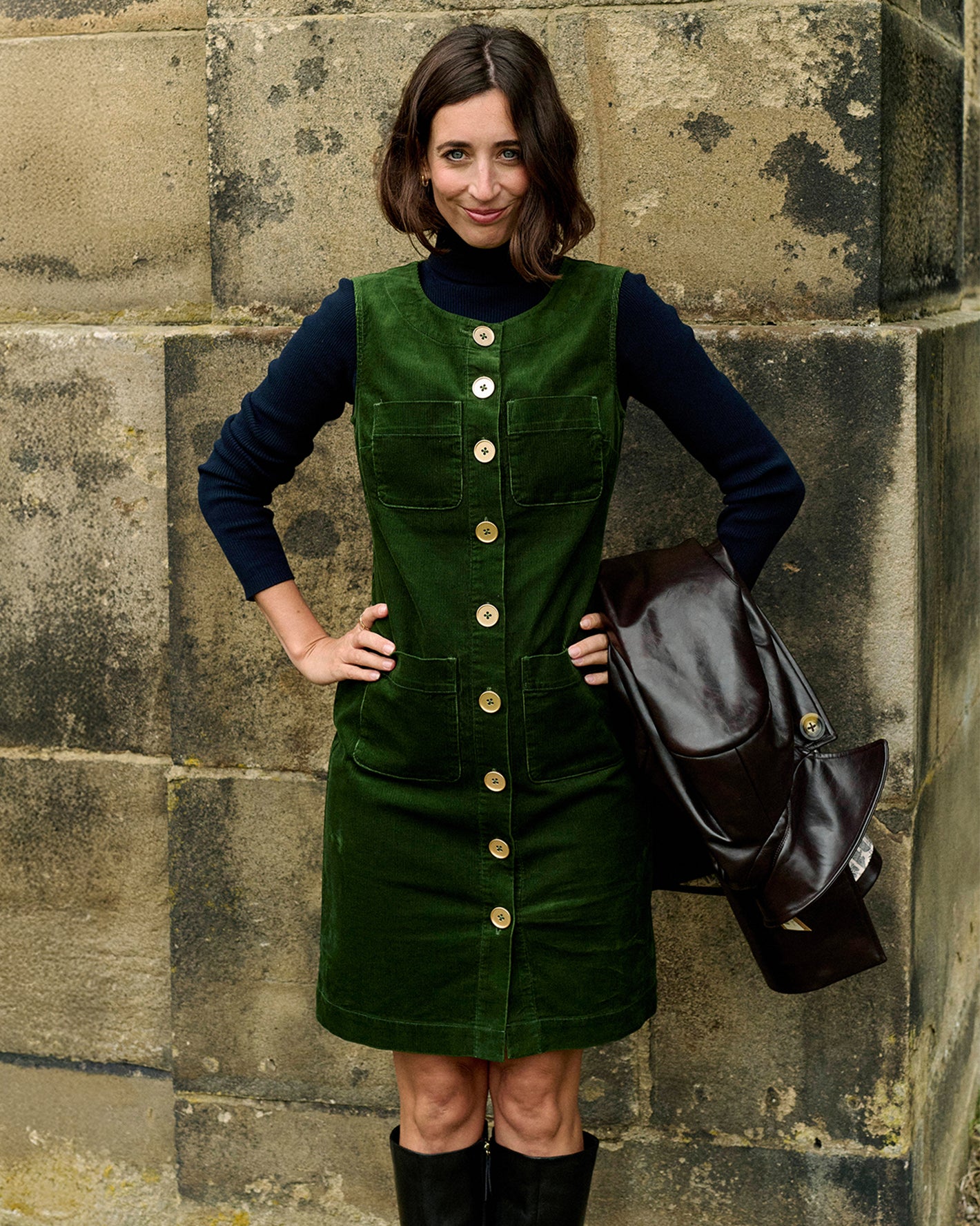 Frau in einem grünen Kleid mit Knöpfen vor einer Steinmauer.