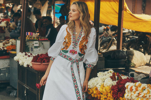 Eine Frau in einem weißen Kleid mit bunten Mustern steht auf einem Markt.